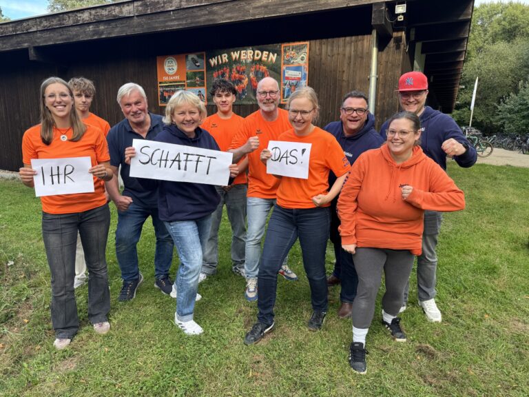 Das Helfer-Team vom Ruderclub Wiking in orangefarbenen Shirts hält Schilder mit „Ihr schafft das!“ hoch