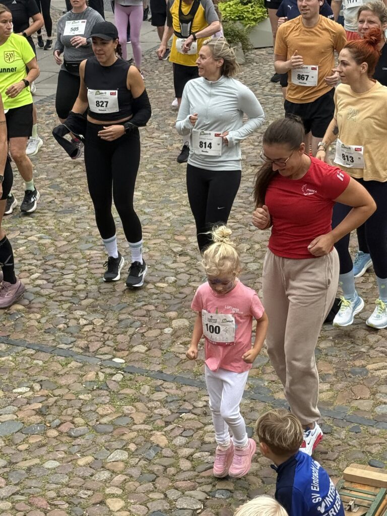 Mittendrin beim Aufwärmen: Läufer:innen mit Startnummern auf dem Kopfsteinpflaster