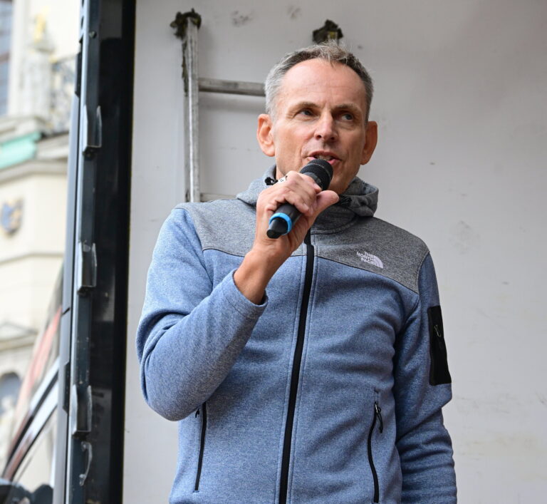 Begrüßung am Mikrofon, im Hintergrund die Rathausfassade