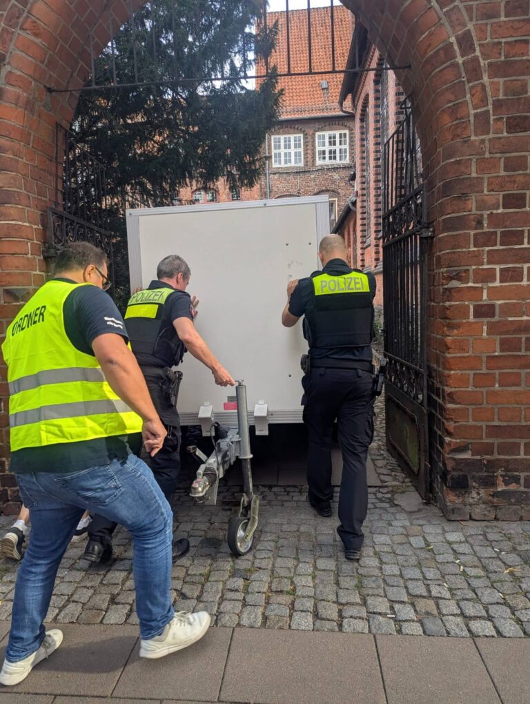 Mit vereinten Kräften: Ein Ordner und zwei Polizisten schieben einen Anhänger durch ein Tor in der Altstadt