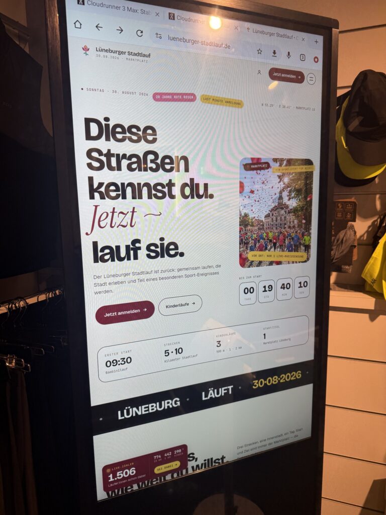 Vorfreude im Schaufenster: Ein Bildschirm zeigt die Stadtlauf-Website mit „Diese Straßen kennst du. Jetzt lauf sie.“